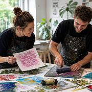 Kursteilnehmende erstellen mit Blättern, Farben und Druckwalzen kreative Monoprints im Atelier.