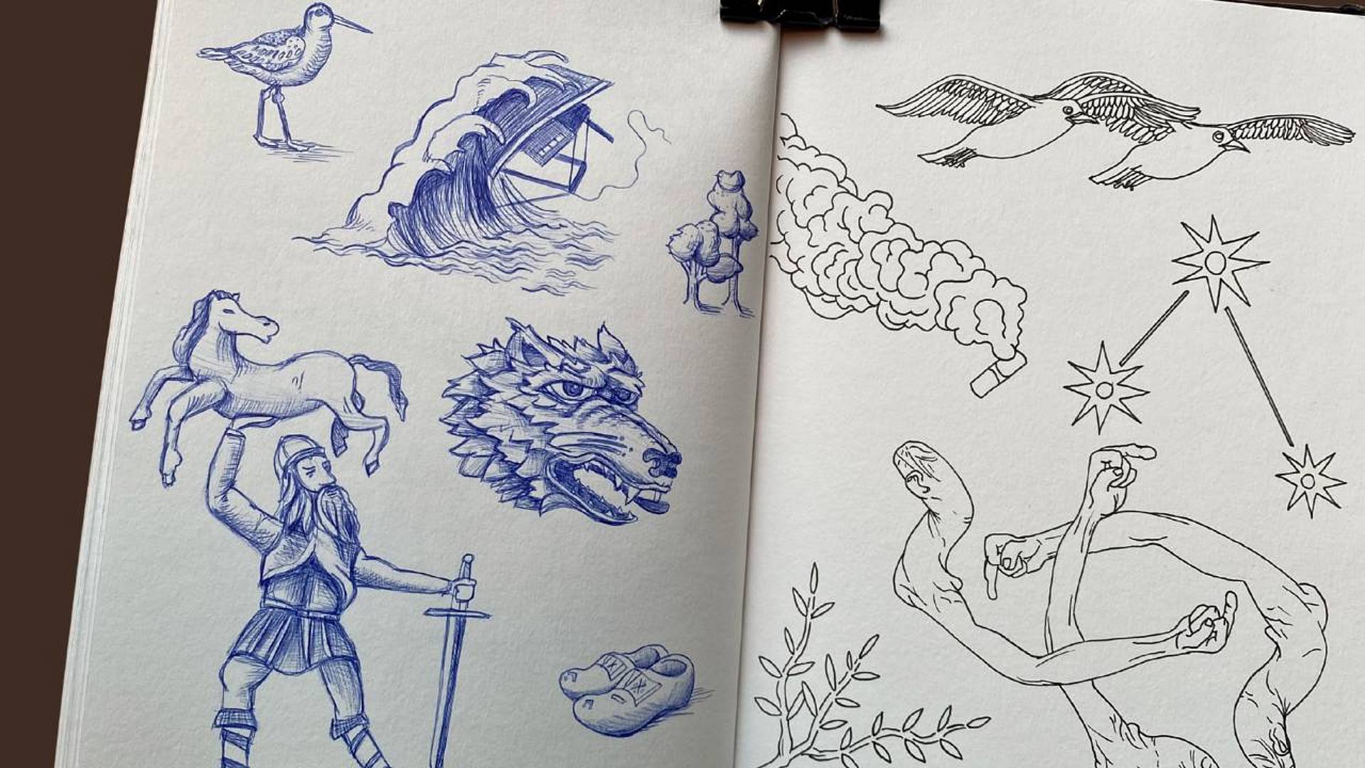 Offenes Skizzenbuch mit blauen Zeichnungen von Tieren, Figuren und Symbolen.
