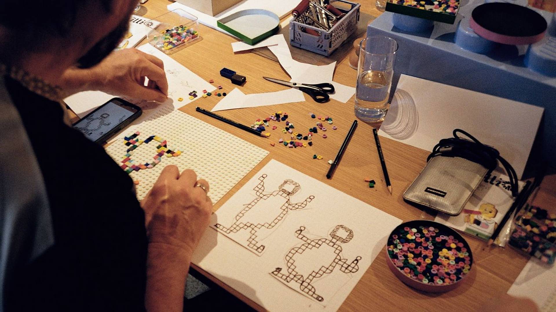 Gestaltung von Lego‑Print‑Motiven in einem Workshop mit Papier‑Vorlagen, Lego‑Steinen und Werkzeugen auf einem Tisch.