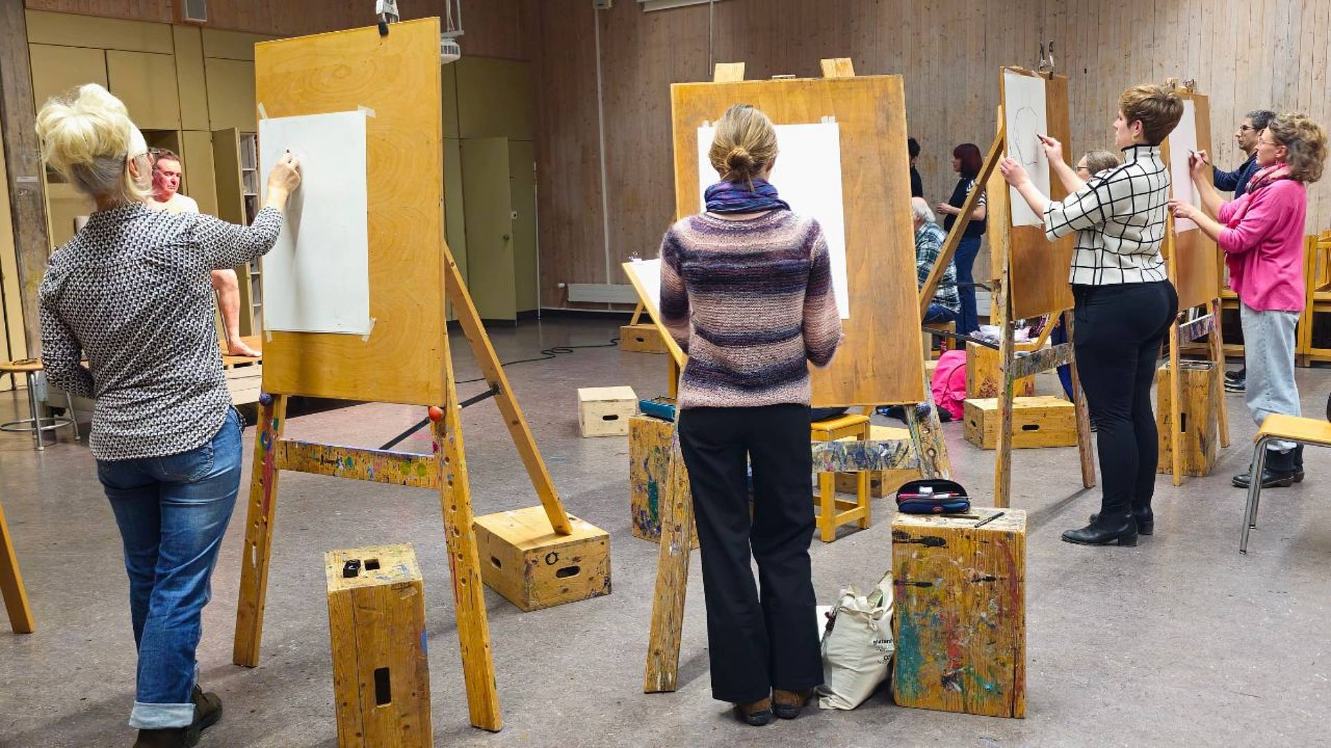 Eine Gruppe zeichnet stehend an Staffeleien in einem grossen Zeichenraum.