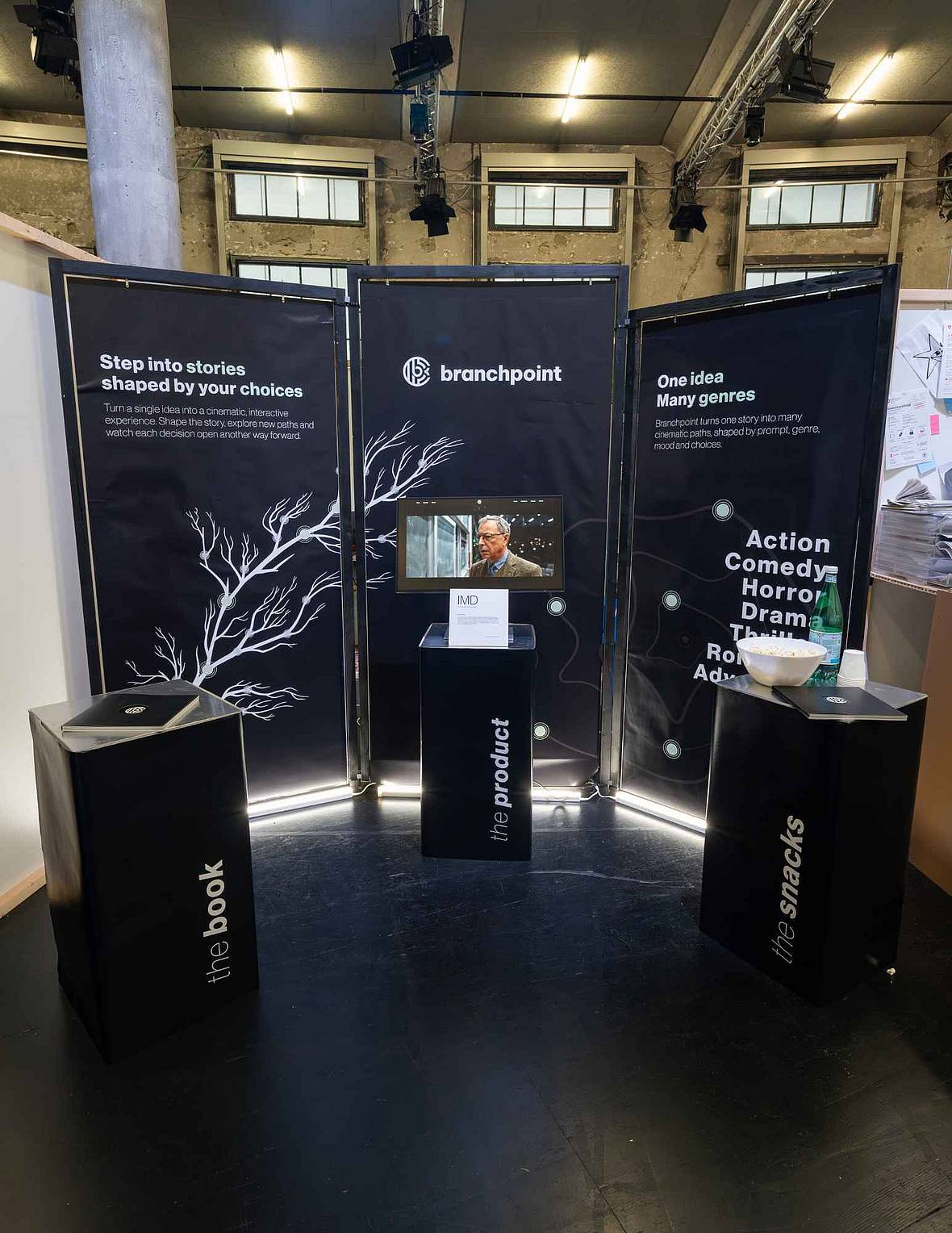 Dunkel gestalteter Branchpoint-Ausstellungsstand mit Infowänden, Bildschirm, Projektbuch und Präsentationselementen.