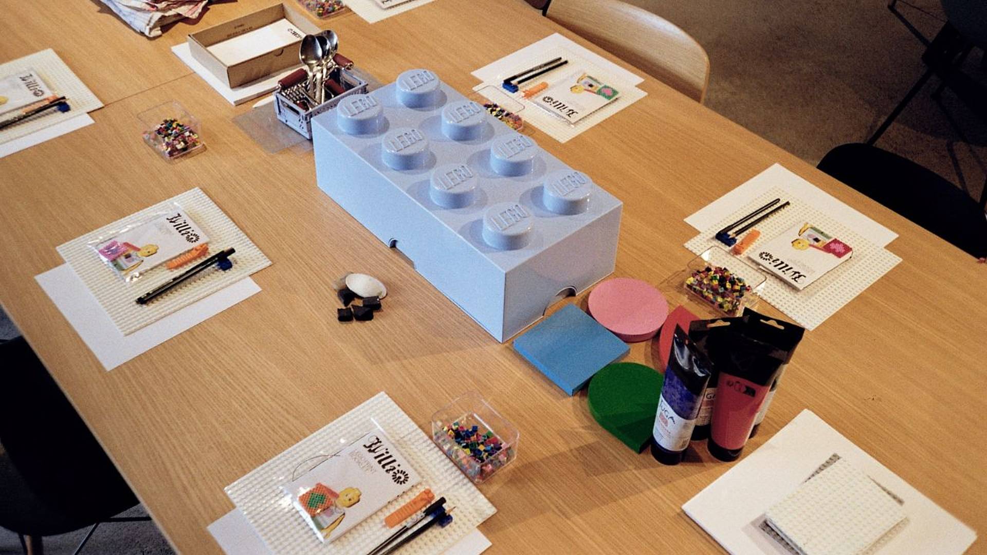 Vorbereiteter Arbeitstisch für Drucken mit Lego‑Steinen, mit Druckmaterialien, Farben und Lego‑Elementen.