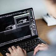 Laptop mit geöffneter Blender‑Software, auf dem ein 3D‑Automodell in einer dunklen Szene modelliert und gerendert wird.
