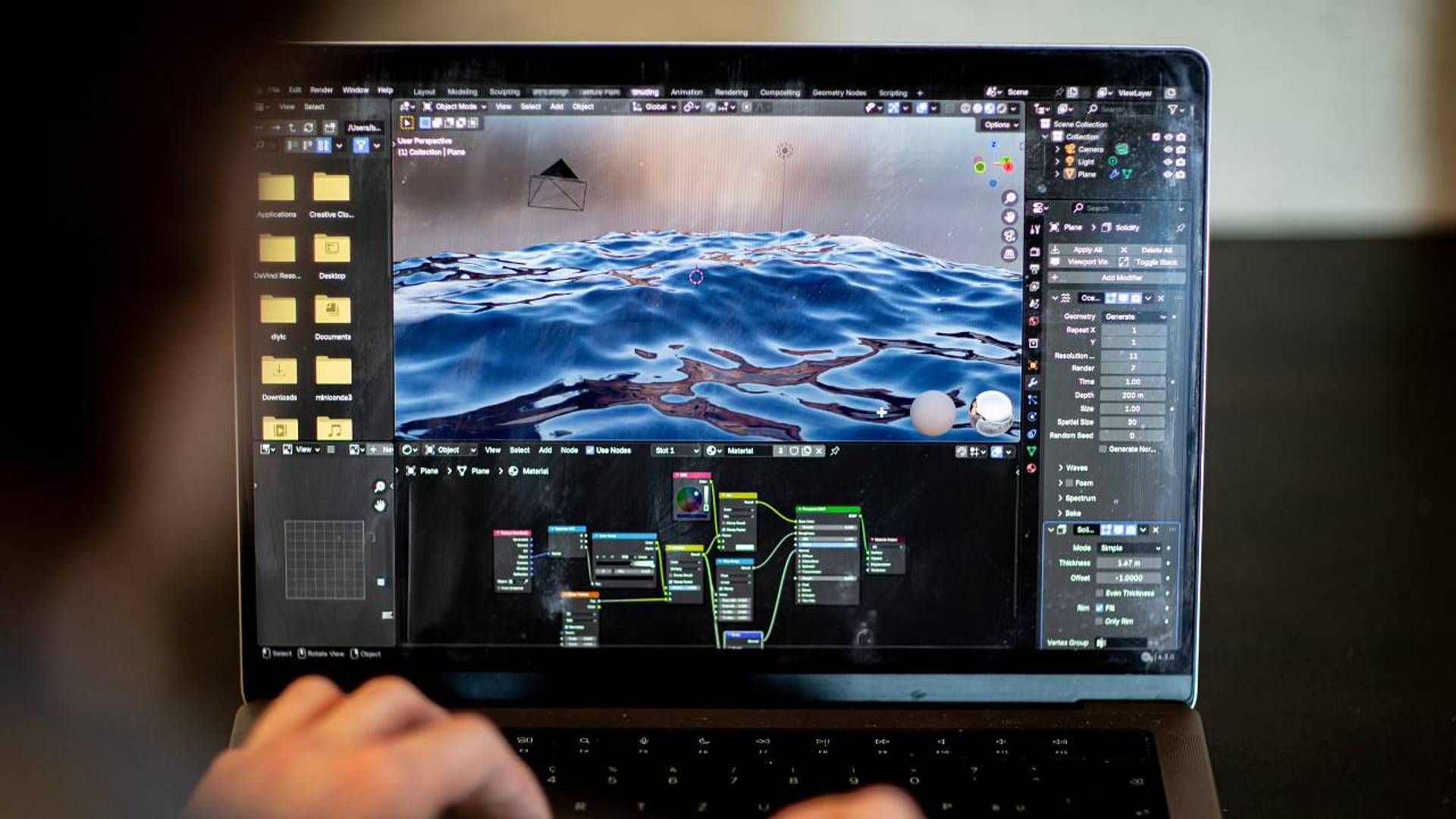 Laptop mit geöffneter Blender‑Software, dargestellt ist eine realistische 3D‑Wasseroberfläche mit Node‑Editor und Materialeinstellungen.
