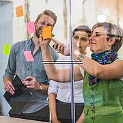 Drei Personen kleben farbige Haftnotizen an eine Glaswand und entwickeln gemeinsam Ideen in einem Workshop.