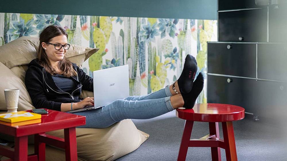 Mädchen arbeitet lächelnd am Notebook, gemütlich sitzend im "Sitzsack"