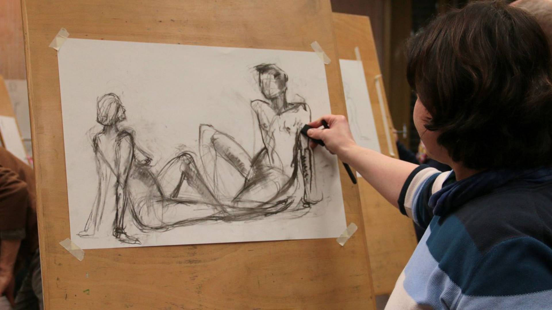 Rückenansicht einer Frau, die an der Staffelei einen Akt skizziert.