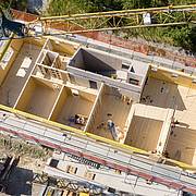 Luftaufnahme eines modernen Holzbaus im Rohbau mit sichtbaren Raumstrukturen und zentralem Treppenhaus.