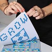 Gedrucktes Muster aus Lego‑Steinen wird über einer Arbeitsfläche mit farbigen Lego‑Elementen präsentiert.