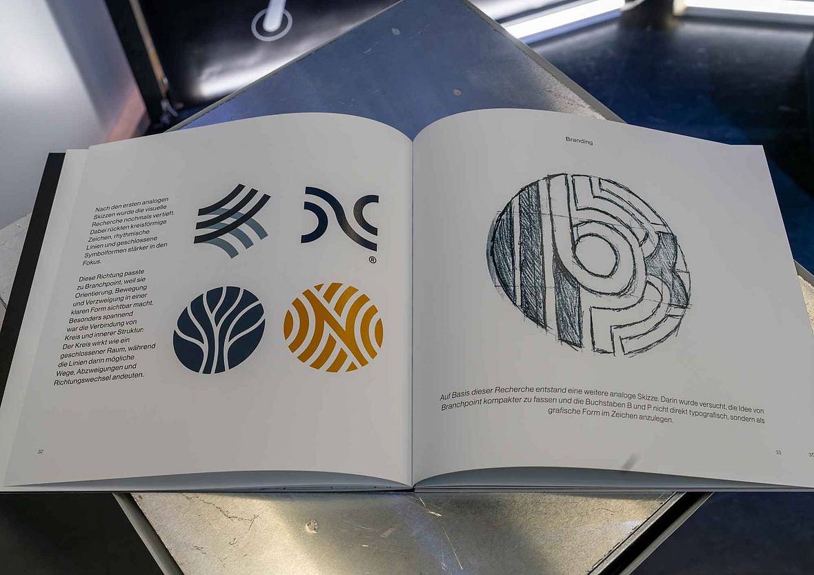 Aufgeschlagenes Gestaltungsbuch mit verschiedenen Logoentwürfen und einer handgezeichneten Skizze des Branchpoint-Logos.