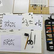 Arbeitsfläche mit beschrifteten Papierkarten, Pinseln, Stiften, Schere und weiterem Kalligrafie‑Werkzeug.
