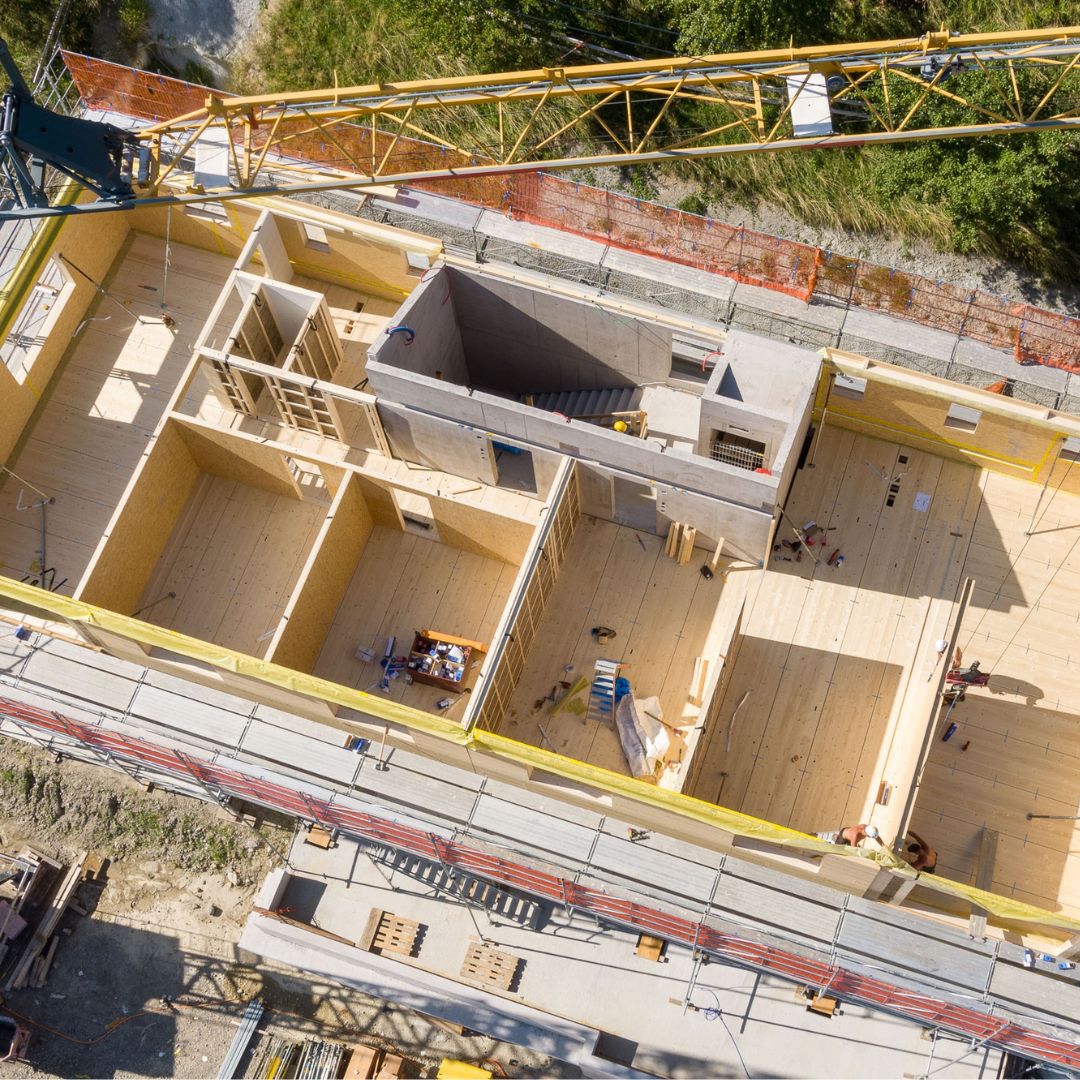 Luftaufnahme eines modernen Holzbaus im Rohbau mit sichtbaren Raumstrukturen und zentralem Treppenhaus.