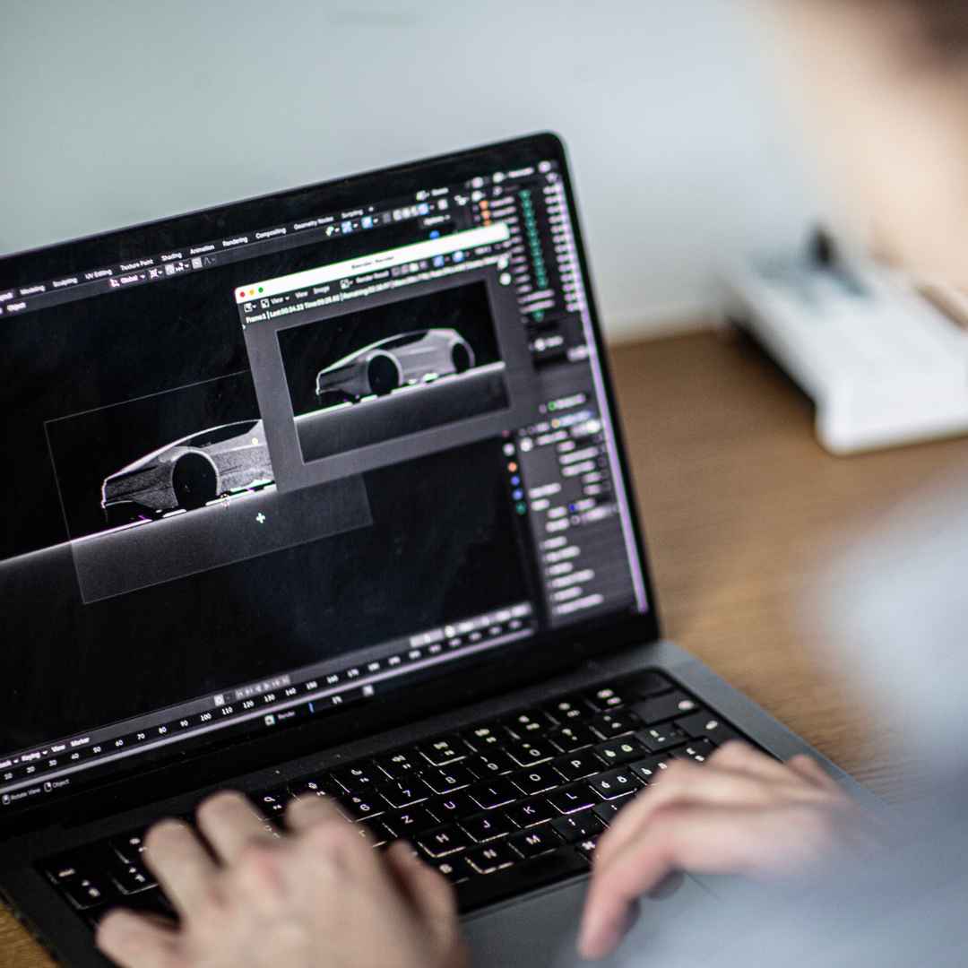 Laptop mit geöffneter Blender‑Software, auf dem ein 3D‑Automodell in einer dunklen Szene modelliert und gerendert wird.