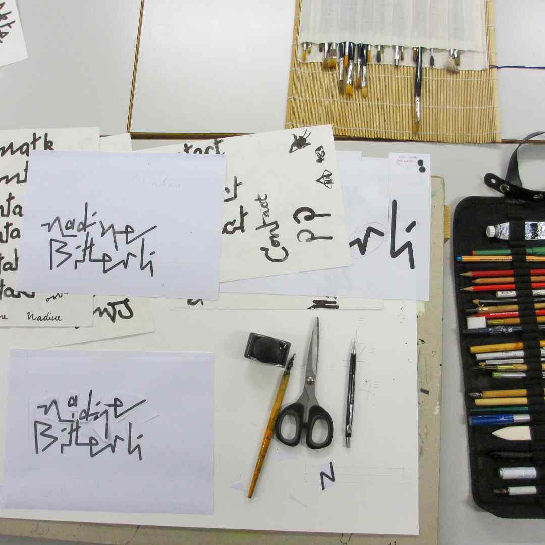 Arbeitsfläche mit beschrifteten Papierkarten, Pinseln, Stiften, Schere und weiterem Kalligrafie‑Werkzeug.
