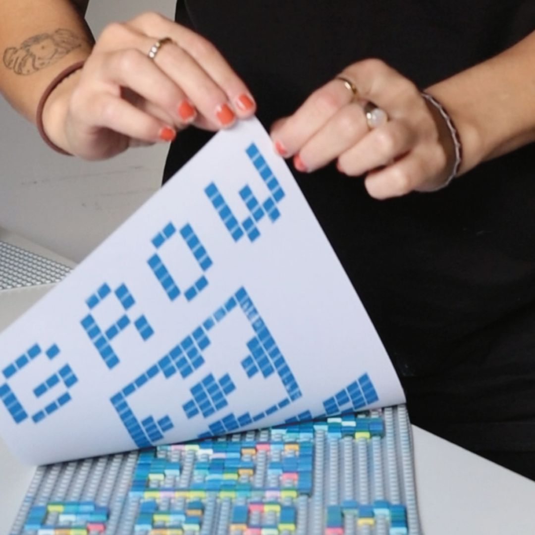 Gedrucktes Muster aus Lego‑Steinen wird über einer Arbeitsfläche mit farbigen Lego‑Elementen präsentiert.