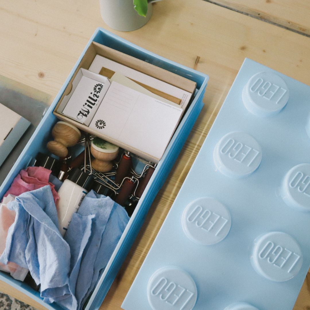 Materialbox für Lego‑Print mit Druckwerkzeugen, Papier, Farben und einem grossen Lego‑Stein als Deckel.
